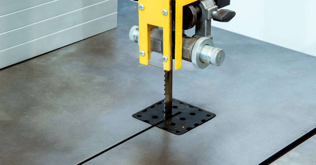 A close-up view of the working table of a vertical band saw. The saw has a blade with toothed edges.