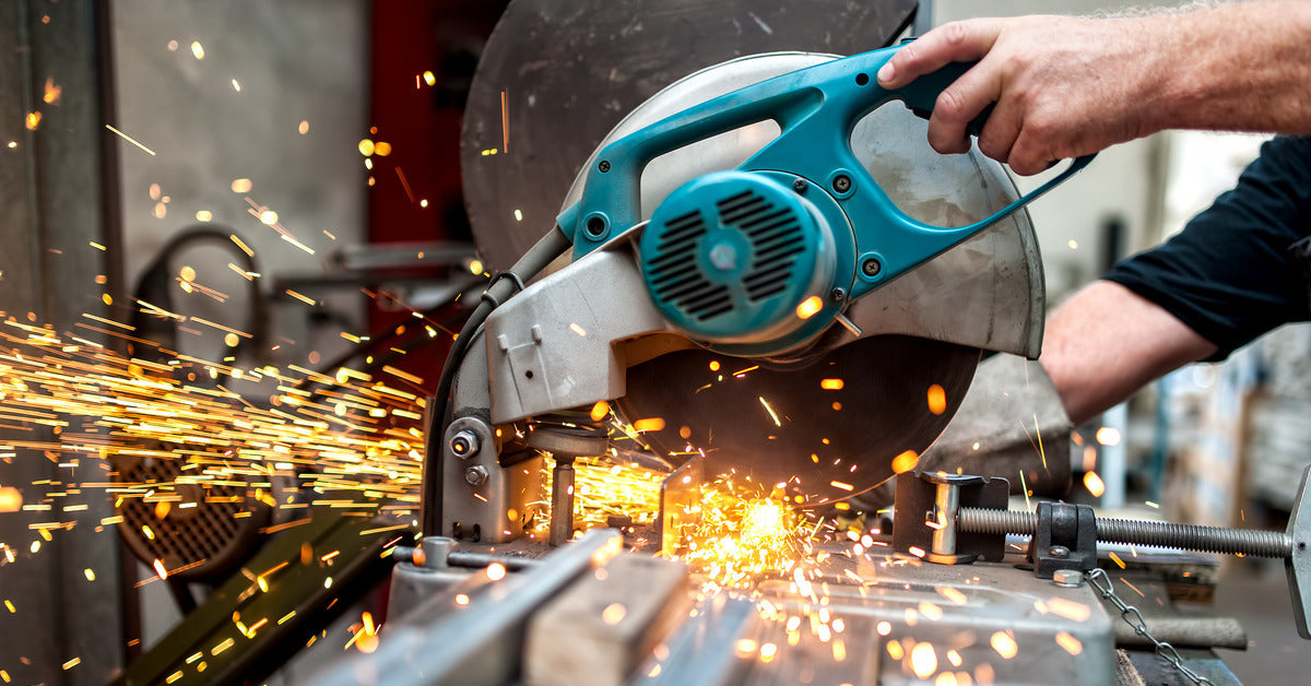 An individual using a circular saw to cut a piece of metal. There are orange and yellow sparks flying through the air.