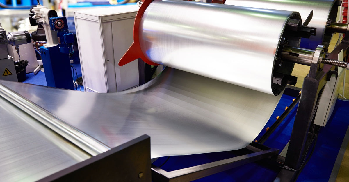 Multiple rolls of sheet metal going through industrial blue-colored metal bending machines in a factory.