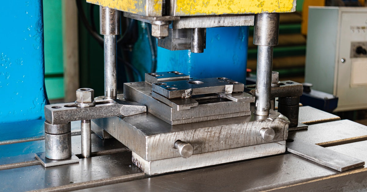 A close-up of an automatic hydraulic press set up as part of a stamping production line. The press has blue and yellow parts.