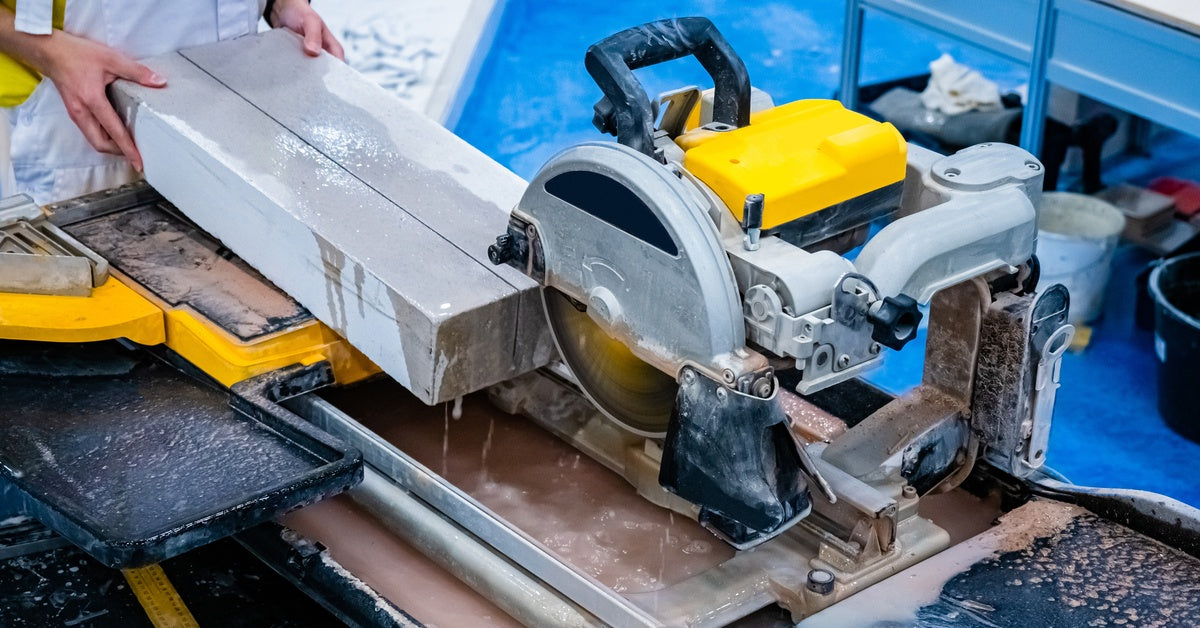 A silver and yellow-colored industrial circular saw cutting through a white concrete slab held by a person.