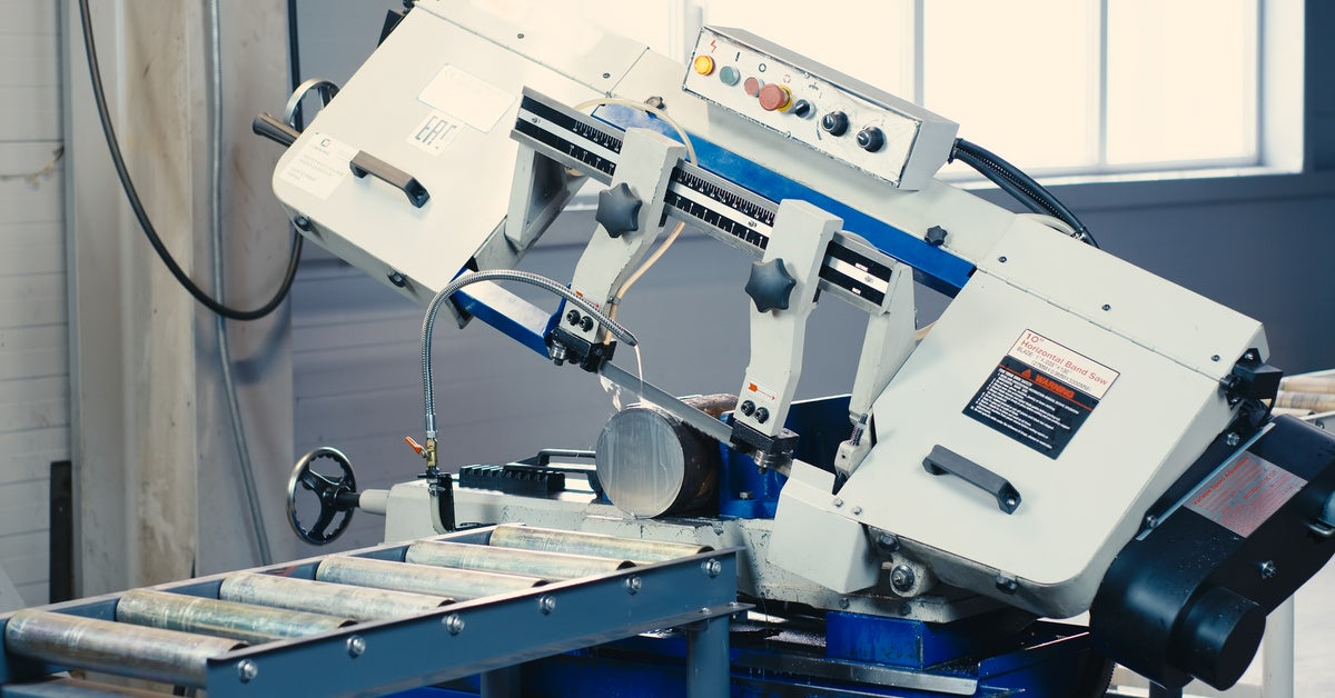 A white and blue-colored horizontal meta band saw cuts through a large aluminum bar placed near the blade.
